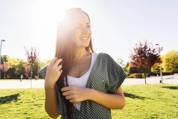 Mutlu gülümseyen genç kız açık uzun saçlarını okşayarak