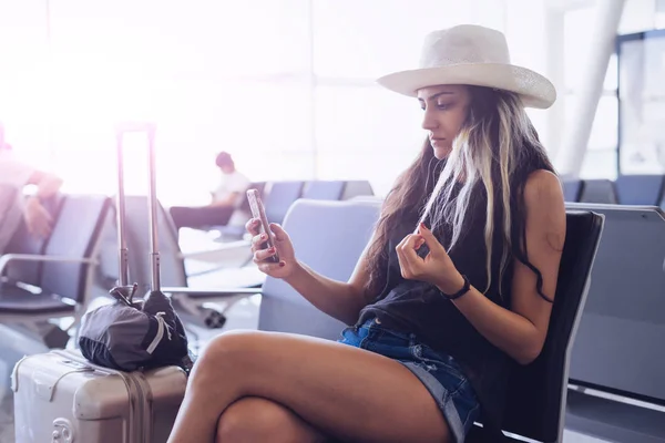 Airport woman in hat on smart phone at gate waiting in terminal. Air travel concept.Looking something in mobile,use  app — Stock Photo, Image