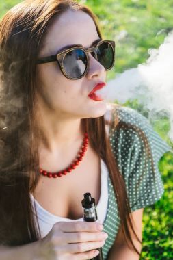 Mutlu moda gülümseyen kadın güneş gözlüğü vape Street, duman Sigara