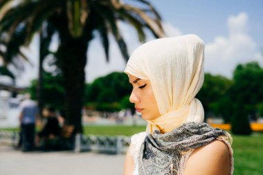 Güzel genç üzücü modern Müslüman kadın avuç fonunda bir yaz parkta oturan bir eşarp