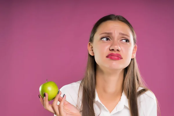 Egy fiatal lány eltúlzott kifejezés almát tart a kezében — Stock Fotó