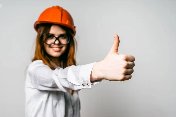 Jovem menina em capacete de construção laranja mostrando polegar — Fotografia de Stock