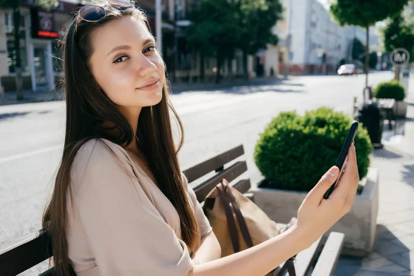 uzağa bakarak onun yüzünü önünde bir telefon tutarak bir bankta oturan genç kız