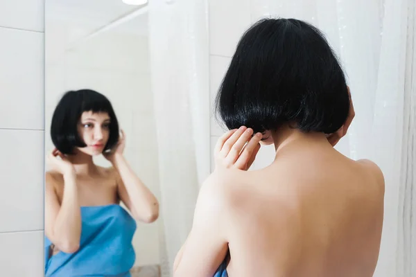Mladá dívka s černými vlasy zkoumá sama v zrcadle, nastavení její vlasy — Stock fotografie