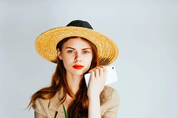 Ragazza in un cappello tiene un telefono in mano su uno sfondo bianco — Foto Stock