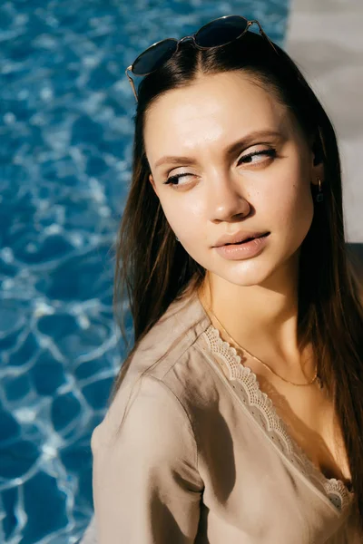Vacker och söt flicka sitter vid poolen tittar fundersamt mot — Stockfoto