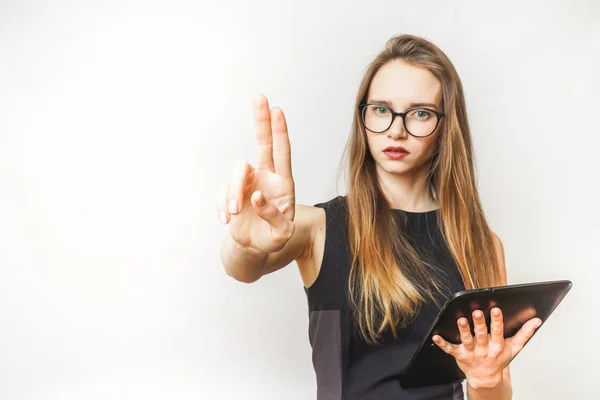 Mürrisch schönes Mädchen mit einer Tablette in den Händen und einem schwarzen Kleid zeigt zwei Finger — Stockfoto