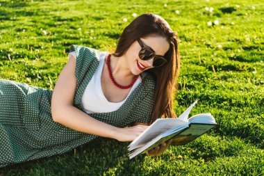 Okuma kadınla çimenlerin üzerinde. Öğrenci park, güneş gözlüğü hazırlanıyor