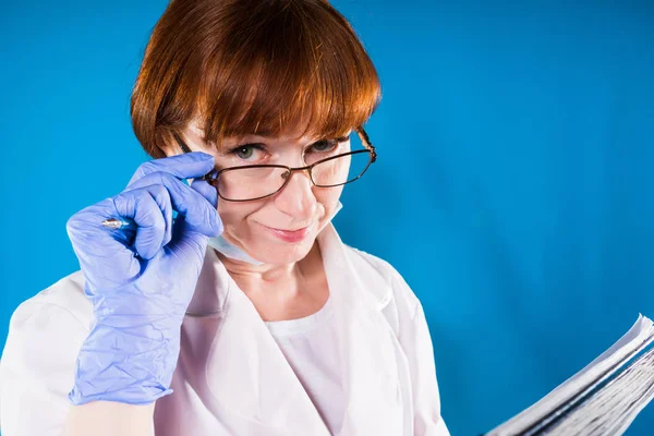 Rödhåriga sjuksköterska i glasögon har en medicinsk kort i hennes händer och ser in i kameran — Stockfoto