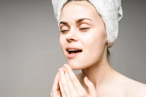 Beautiful cute girl after shower with towel on her head smears cream face — Stock Photo, Image