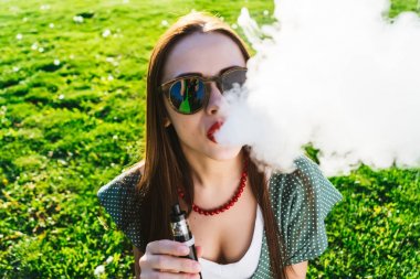Mutlu moda gülümseyen kadın güneş gözlüğü vape Street, duman Sigara