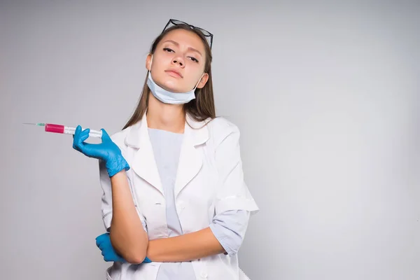 Una ragazza carina in un accappatoio medico bianco guarda con rabbia la fotocamera e tiene una siringa tra le mani — Foto Stock