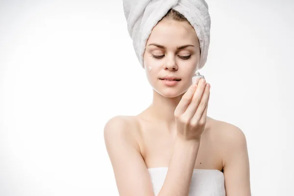 Ragazza dopo la doccia con un asciugamano bianco sulla testa spalmato crema per il viso — Foto Stock