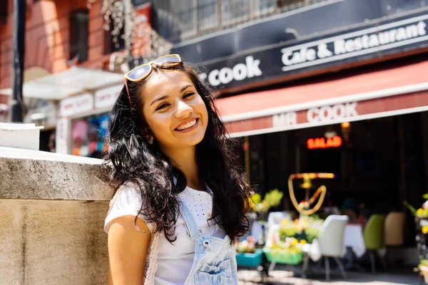 Söt flicka med mörkt hår leende på gatan. Leende flicka i solglasögon över urbana staden gatan bakgrund. — Stockfoto