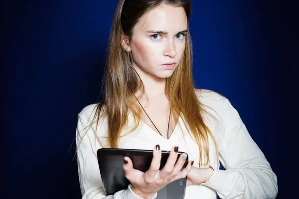 Menina com uma expressão surpresa detém um tablet em um fundo azul — Fotografia de Stock