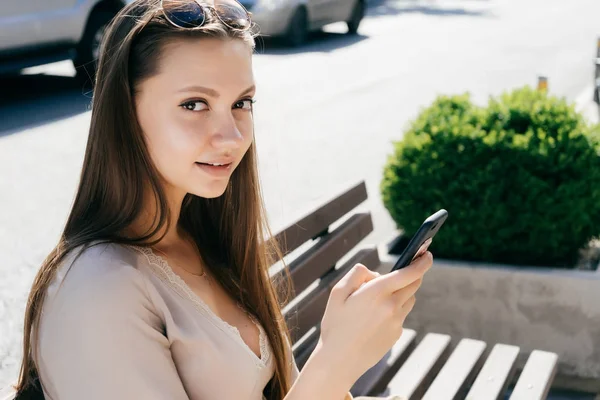 Chica con un teléfono en las manos sonriendo mirando hacia otro lado — Foto de Stock
