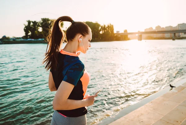 Girl on a sunset background performs an evening run with a phone in hands — Stock Photo, Image