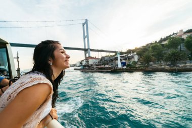 Mutlu genç traveler kız tam görünümünde, boğaz üzerinde günbatımı gülümseyerek. Modern köprü