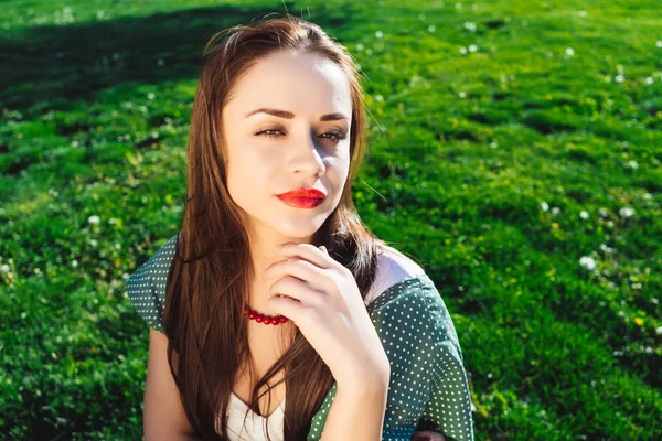 Femme sceptique aux lèvres rouges assise sur une herbe — Photo