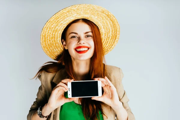 Lány kalapban mosolyogva gazdaság telefon képernyő előtt — Stock Fotó
