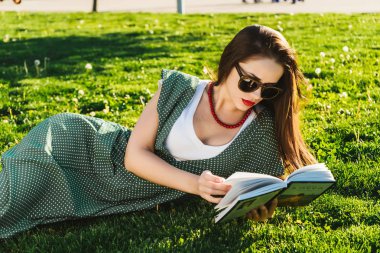 Okuma kadınla çimenlerin üzerinde. Öğrenci park, güneş gözlüğü hazırlanıyor