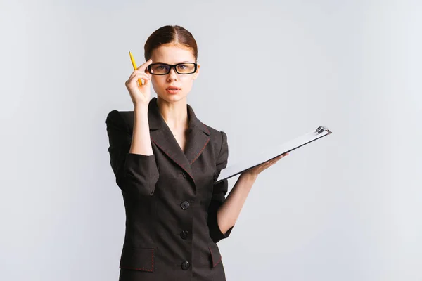 Внимательная деловая леди в черном костюме держит папку и ручку, держит очки и смотрит прямо в камеру — стоковое фото