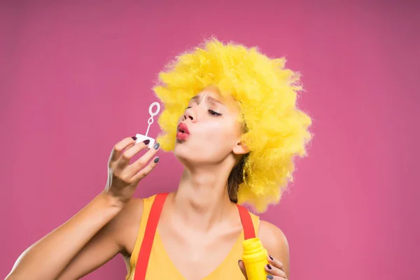Funny girl in a bright yellow wig blowing soap bubbles — Stock Photo, Image
