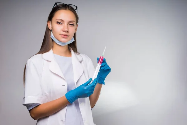 Lovely girl in a medical dressing gown holds a syringe with an antibiotic in her hands — Stockfoto