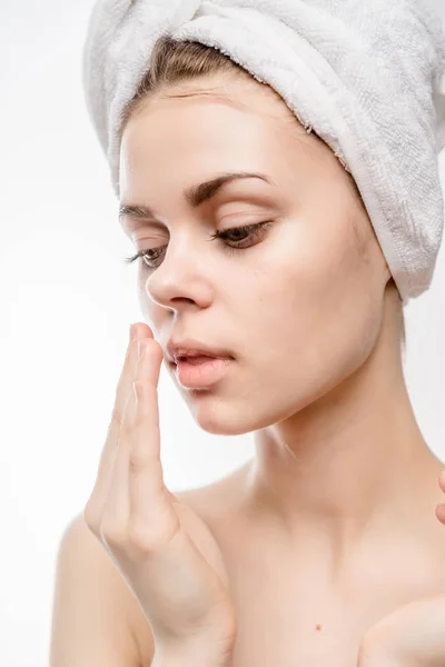 A girl after a shower with a towel on her head is going to smear her face with cream and looks down — Stock Photo, Image