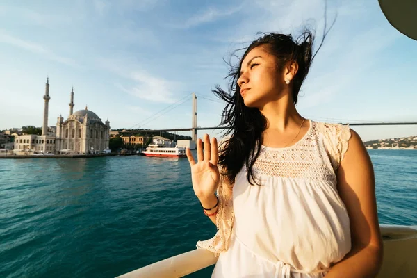 Düşünceli bir kız bir teknede boğaz bir cami ve bir köprü arka planda yelken