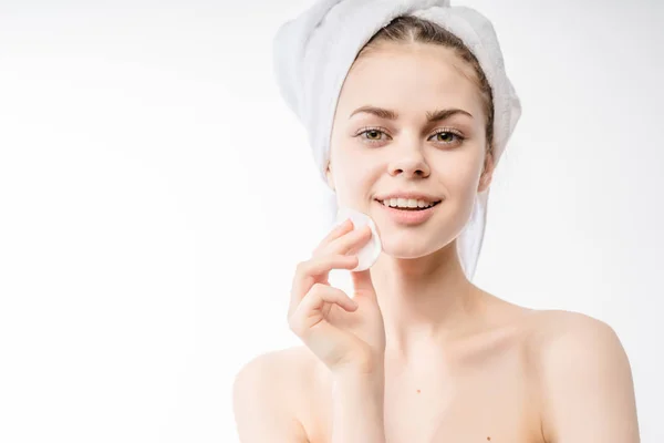 Chica después de la ducha con una toalla en la cabeza sonriendo y limpiándose la cara con una esponja —  Fotos de Stock