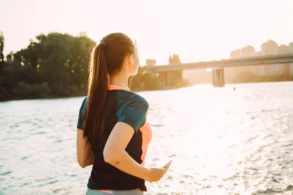 Flickan går längs flodstranden och lyssnar på musik i hörlurar — Stockfoto