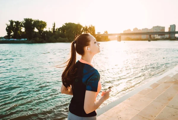 Tjej jogging på flodstranden lyssnar på musik i hörlurar — Stockfoto