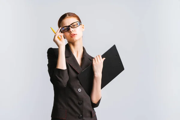 Серьезная девушка в очках и в костюме держит карандаш и листы бумаги a4 — стоковое фото
