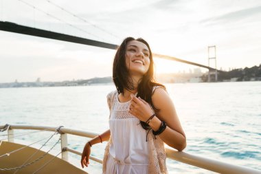Günbatımı ve gülüyor modern bir köprünün altında bir güzel Latin kız bir yatta yelken