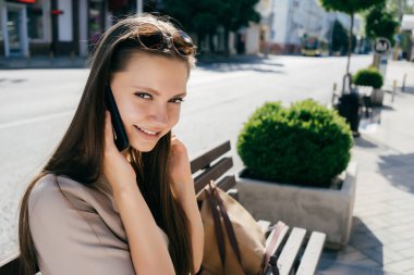 telefonda konuşurken bankta oturmuş gülümseyen genç kız