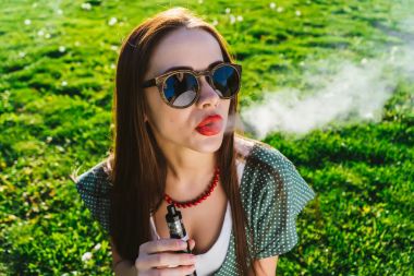 Mutlu moda gülümseyen kadın güneş gözlüğü vape Street, duman Sigara