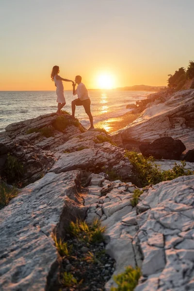 Молодая пара наслаждается романтикой на каменном пляже на фоне заката — стоковое фото