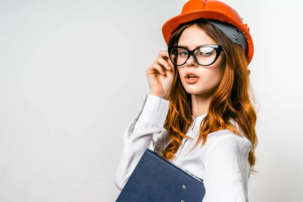 Jovem secretária menina em óculos e um capacete de construção laranja — Fotografia de Stock