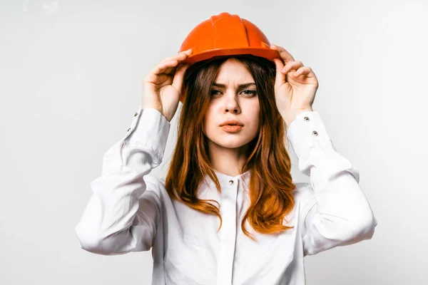 Linda menina ruiva em uma camisa branca e vestindo um capacete laranja olha para a câmera — Fotografia de Stock