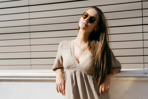 Una ragazza con gli occhiali da sole appoggiata al davanzale di una finestra sulla strada — Foto Stock