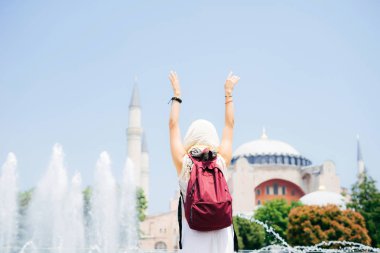 Bir eşarp ile cami ve Çeşme bir arka plan üzerine bir sırt çantası içinde tanınmayan bir kadın. Yaz tatili, gezgin