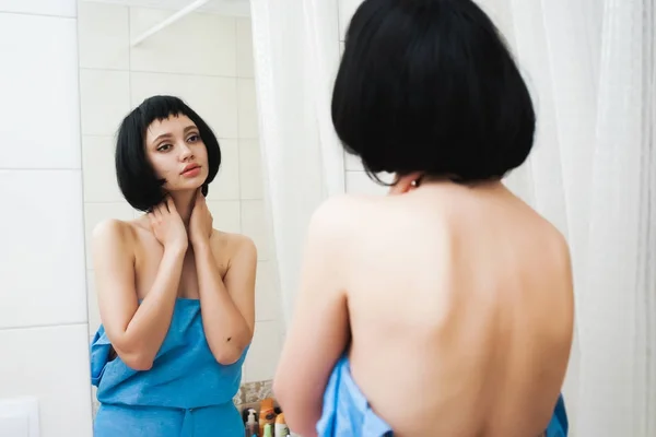 Дівчина з чорним волоссям в рушнику оглядає себе у дзеркалі — стокове фото