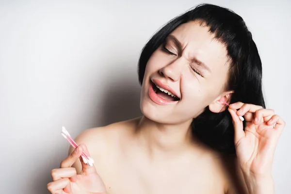 Menina com cabelo preto limpa os ouvidos em um fundo branco — Fotografia de Stock