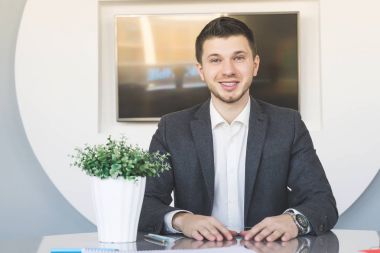 masada oturan gülümseyen iş elbiseli genç adam