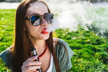 Mutlu moda gülümseyen kadın güneş gözlüğü vape Street, duman Sigara