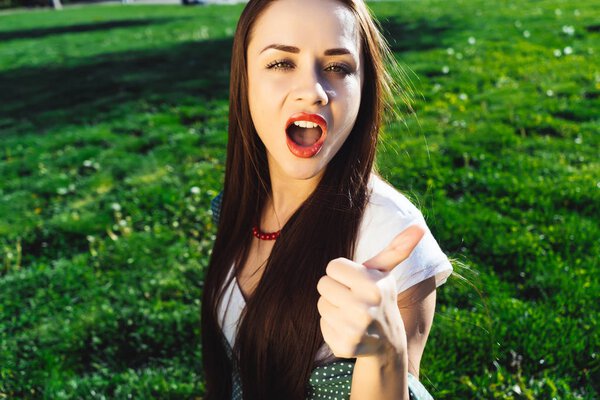 Passionate woman shows thumbs up outdoor,sit on grass