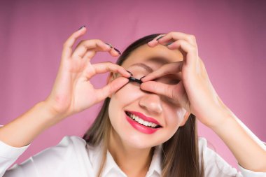 Kız gülümseyerek ve sahte kirpik taşırsanız pembe bir arka plan üzerinde