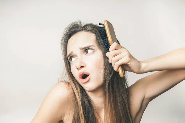 Menina bonito penteia cabelos longos com um pente de madeira e é desagradável para ela — Fotografia de Stock