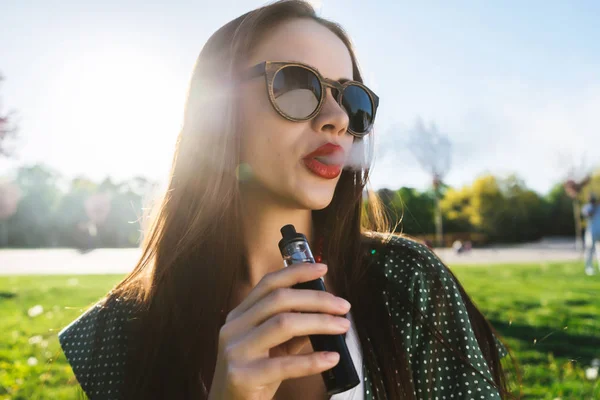 Feliz moda sonriente Mujer en gafas de sol fumar vapor en la calle, humo — Foto de Stock